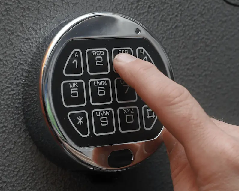 A finger pressing the electronic keypad on a safe door